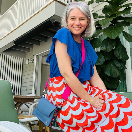 Woman in a blue top and red and white patterned skirt sitting on a green chair outdoors.