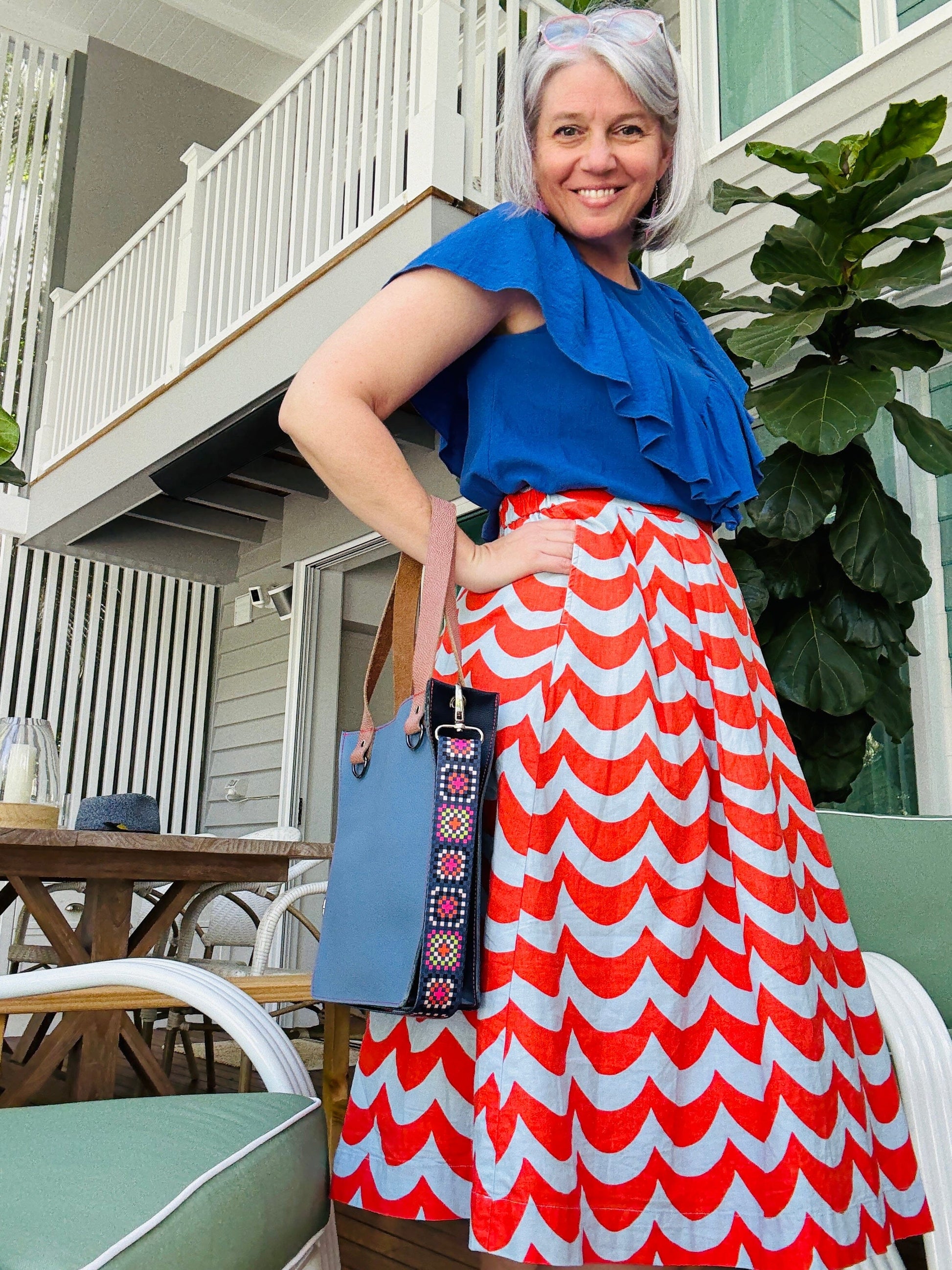 Woman in a blue top and red and white patterned skirt standing outdoors.